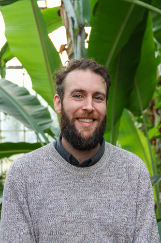 Man smiling in front of large green leaves